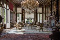 <p>Armchairs and tables stand beneath chandeliers as 19th century portraits in ornate frames adorn the walls of a sitting room inside the villa. </p>