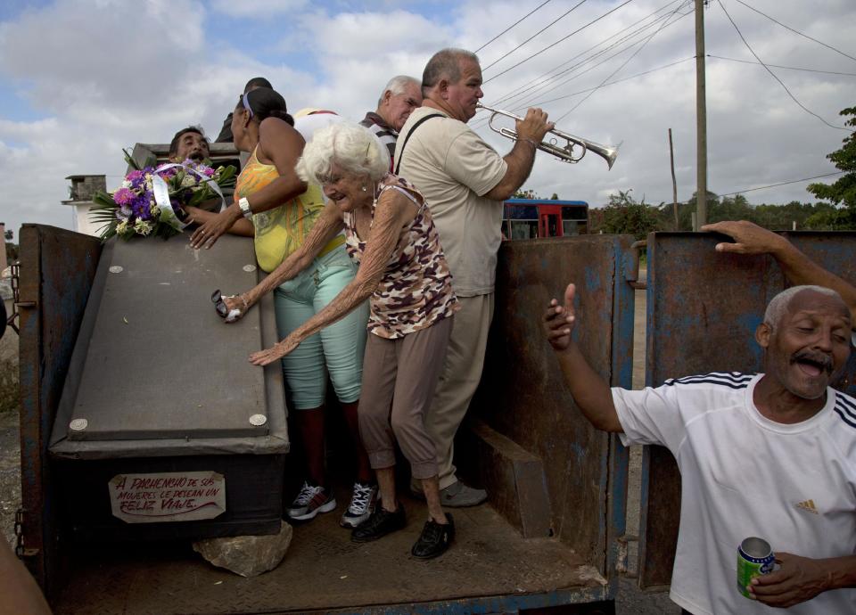 In this Feb. 5, 2014 photo, Divaldo Aguiar, who plays the part of Pachencho, left, lies inside a coffin as Carmen Zamora, who plays his widow, center, stands near the coffin, during the town's annual tradition, known as the Burial of Pachencho, at a cemetery in Santiago de Las Vegas, Cuba. A tractor pulls a trailer slowly through the streets to the cemetery in the early morning carrying Aguiar in a coffin, along with a four-piece tropical band and the white-haired woman pretending to be the bereaved widow weeping loudly for the "deceased." (AP Photo/Enric Marti)