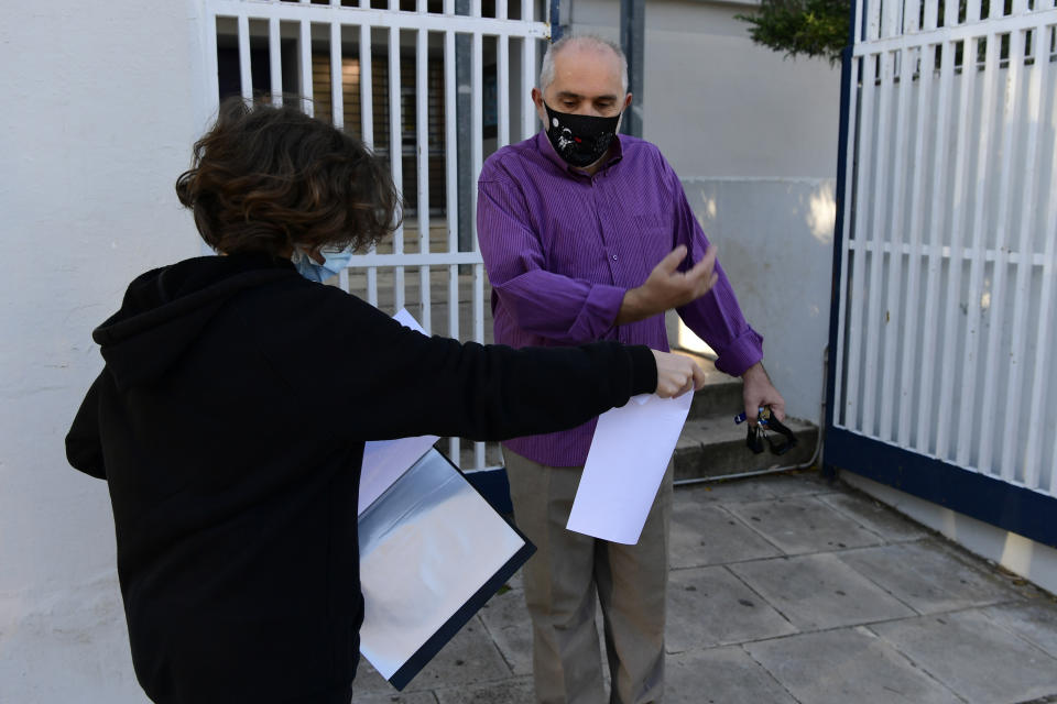 A student shows his document stating a negative COVID-19 self-test as a teacher lets him to enter the school in Athens, Monday, May 10, 2021. More than 1.1 million pupils and 127,300 teachers returned to school on Monday as primary and junior high school reopened its doors with mandatory home self-tests. (AP Photo/Michael Varaklas)