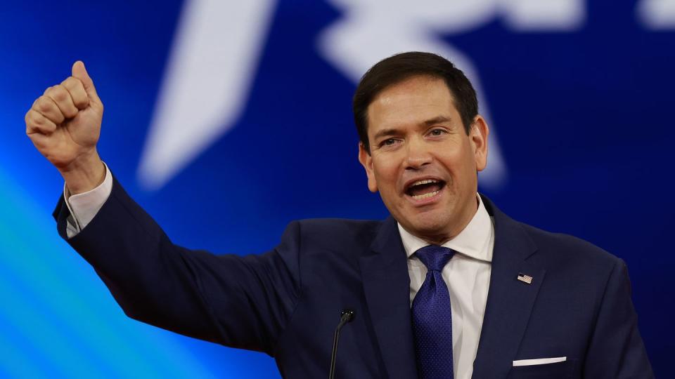 marco rubio raising and making a fist with his right arm as he speaks behind a glass podium