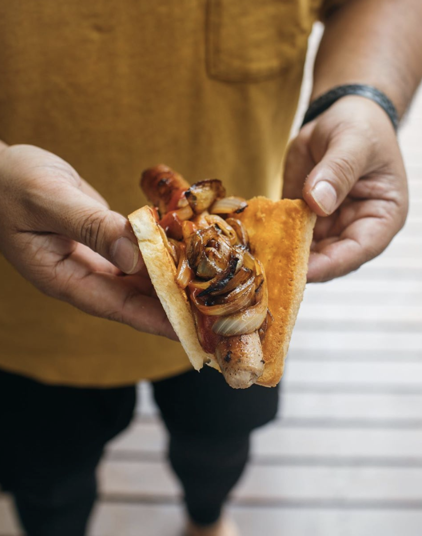 Adam Liaw holds a cheesy sausage sandwich.