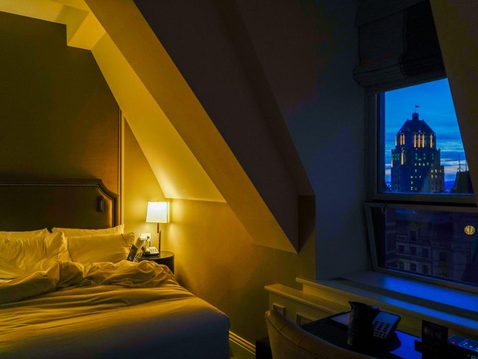 Inside a dark hotel room with a bed on oneside and a view of architecture in Quebec city at night on the other