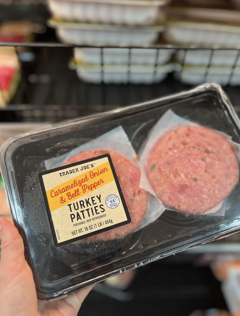 A hand holds a package of Trader Joe's Caramelized Onion & Bell Pepper Turkey Patties.