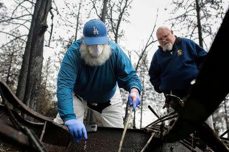 FILE PHOTO: Stanley Miniszewski Sr. uses a burnt golf club to look for a pair of expensive dentures in the remains of his RV after returning for the first time since the Camp Fire forced him to evacuate as his friend Merrill Jackson looks on at Pine Ridge Park in Paradise, California, U.S. November 22, 2018. REUTERS/Elijah Nouvelage/File Photo