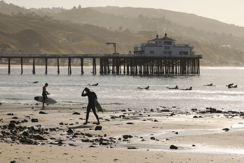 MALIBU, CA - MAY 13: Surfers take advantage of the low tide swell at Malibu Surfrider Beach next to the Malibu Pier Wednesday morning as Los Angeles County Beaches reopened for active use only. The beaches have been closed for two months due to the coronavirus Covid-19 pandemic and remained off limits even as the coastline reopened for active use in Orange County. Beachgoers will have to wear masks and maintain a six-foot buffer between themselves and others under continued social distancing requirements. Parking lots, piers and boardwalks will remain closed. Malibu Pier on Wednesday, May 13, 2020 in Malibu, CA. (Al Seib / Los Angeles Times)