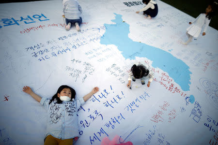 Children play on a unification flag decorated with messages wishing for a successful inter-Korean summit during a rally in central Seoul, South Korea, April 21, 2018. REUTERS/Kim Hong-Ji