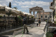 FILE - In this Saturday, May 23, 2020 file photo, a man sprays water at umbrellas outside a tavern at Plaka district, in Athens, as the restaurant prepares for reopening. Greece's Prime Minister Kyriakos Mitsotakis said Wednesday April 21, 2021, the country's tourism industry will open on May 15 when a ban on travel between different regions in the country will be lifted, adding that restaurants and cafes will also be allowed to reopen outdoor areas starting on May 3. (AP Photo/Yorgos Karahalis, File)