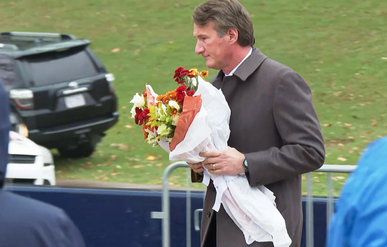 In this image from video, Virginia Gov. Glenn Youngkin brings flowers to a memorial service at the University of Virginia, Tuesday, Nov. 15, 2022, in Charlottesville, Va. A University of Virginia student and former member of the school's football team fatally shot three current players as they returned from a field trip, authorities said, setting off panic and a 12-hour lockdown of the campus until the suspect was captured Monday. (AP Photo/Nathan Ellgren)
