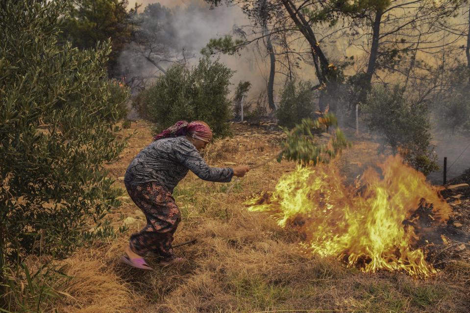 A woman tries to stop an advancing wildfire in Kacarlar village near the Mediterranean coastal town of Manavgat, Antalya, Turkey, Saturday, July 31, 2021. The death toll from wildfires raging in Turkey's Mediterranean towns rose to six Saturday after two forest workers were killed, the country's health minister said. Fires across Turkey since Wednesday burned down forests, encroaching on villages and tourist destinations and forcing people to evacuate. (AP Photo)