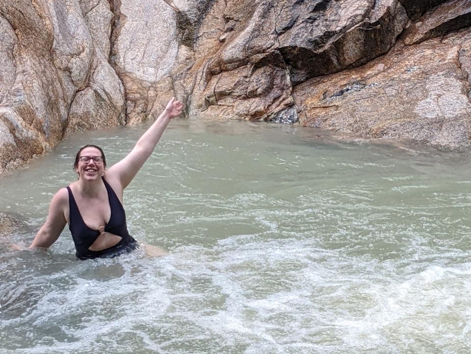 A woman taking a picture with her arm up while in a river-like body of water.