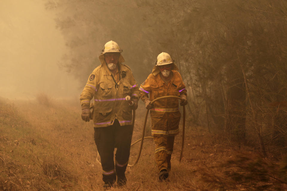 New South Wales firefighters drag their water hose after putting out a spot fire on the state's south coast. (Photo: ASSOCIATED PRESS)
