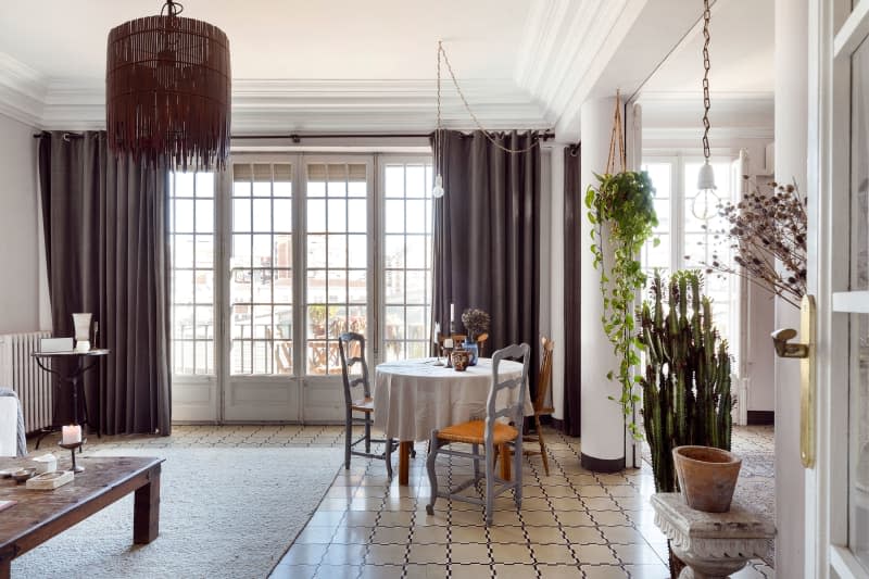 View of wall of window doors shows small dining table and plants at entryway.