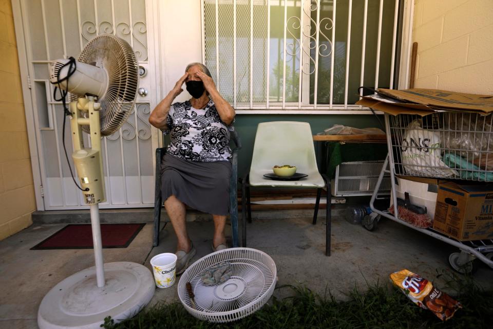 PACOIMA, CA - AUGUST 3, 2021 - - Felisa Benitez, 86, wipes the sweat from her brow while taking a break from cleaning her stand-up electrical fan on the porch of her home where temperatures reached 99 degrees at the San Fernando Gardens Public Housing in Pacoima on August 4, 2021. Benitez, who lives alone, tries to only use fan to cool herself even though she has an AC unit, to the right, at her place. She is on a limited budget and uses the AC sparingly to avoid a huge electrical bill that she cannot afford to pay. Benitez, who has lived at the gardens since the 90s, spends a great deal of her day seated in the shade of her porch. According to Los Angeles County Coroners and Medical Offices, hundreds of heat-related deaths reviewed by the Times showed the victims included seniors who died alone in apartments without air conditions, or with the thermostat off. (Genaro Molina / Los Angeles Times via Getty Images)