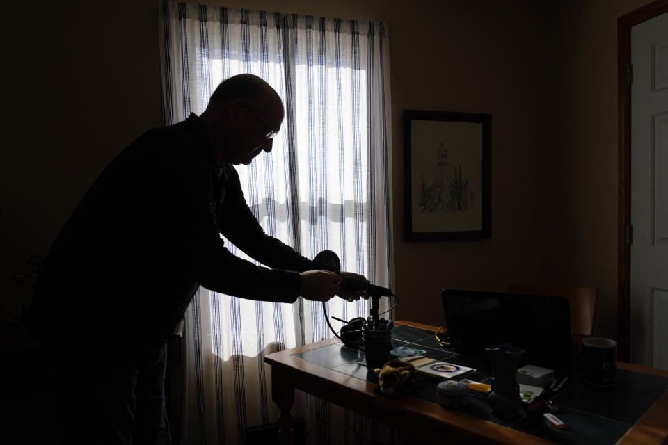 Roger Strukhoff 67, stands in silhouette cleaning off his home office desk Thursday, Jan. 20, 2022, in his DeKalb, Ill., home. Strukhoff was being treated for intestinal bleeding at a hospital outside Chicago this month when he suffered a mild heart attack. Normally, the medical staff would have sent Strukhoff to the intensive care unit, but, overrun with COVID-19 patients, the staff instead had to wheel a heart monitor into his room and quickly administer nitroglycerin and morphine. (AP Photo/Charles Rex Arbogast)