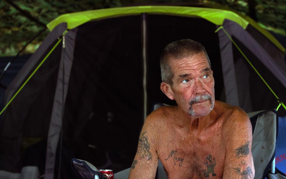 William Honeker enjoys the cool evening air as he sits outside his tent. A homeless camp in the woods in Toms River on August 10, 2023