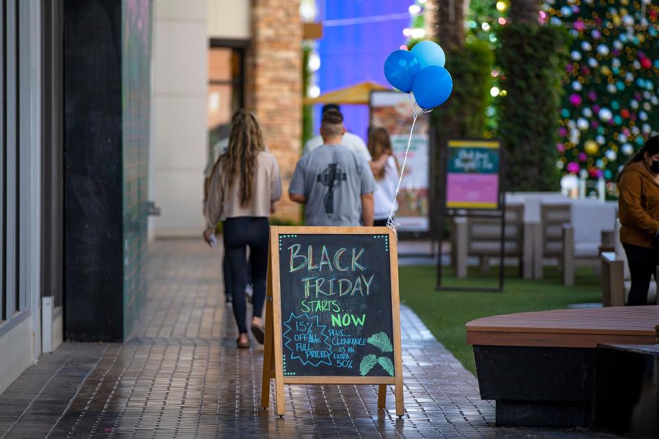 A chalkboard sign reading, "Black Friday starts now," sits outside a store as shoppers walk by at Tempe Marketplace on Nov. 26, 2021.