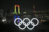 The illuminated Olympic rings float in the water as the Rainbow Bridge and the Tokyo Tower are visible in the distance Friday, Jan. 24, 2020, in the Odaiba district of Tokyo. Tokyo put on a flashy fireworks display on Friday to mark the 6-months-to-go milestone for this summer's Olympics. (AP Photo/Jae C. Hong)