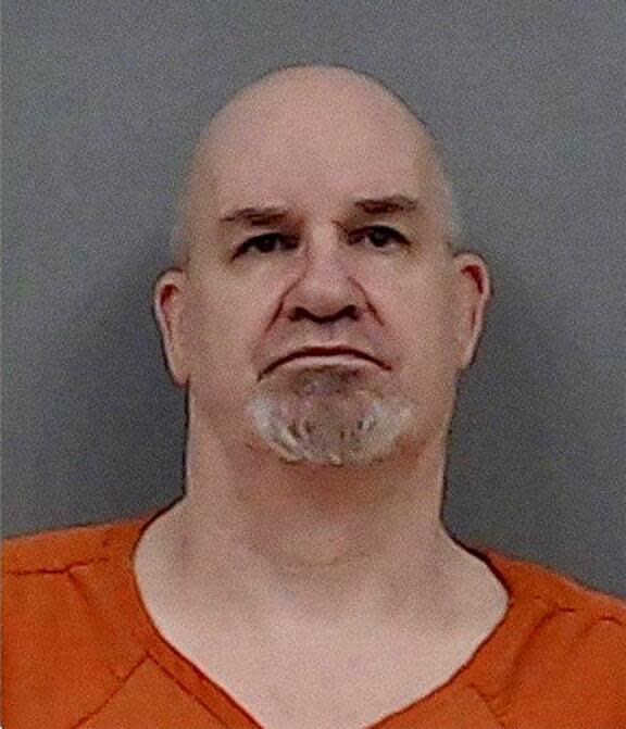 A man with shaved head and chin hair in an orange jail uniform