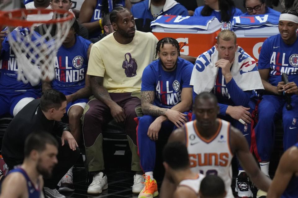 Kawhi Leonard, in yellow, sits on the Clippers bench during Game 3 against the Phoenix Suns on April 20 at Crypto.com Arena.