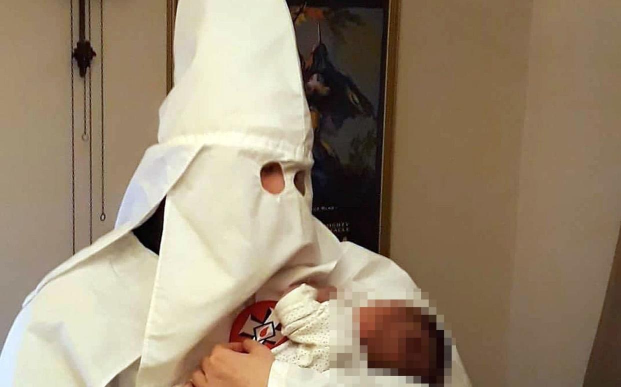 A photo shown to jurors at Birmingham Crown Court, allegedly showing Adam Thomas, posing with his new-born baby, whilst wearing the hooded white robes of the Ku Klux Klan  - PA