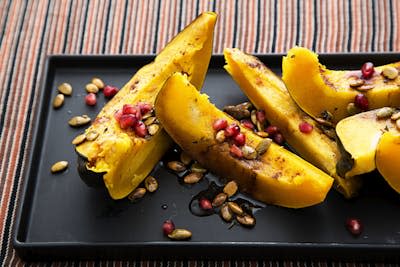 Roasted acorn squash slices strewn with nuts and pomegranate seeds