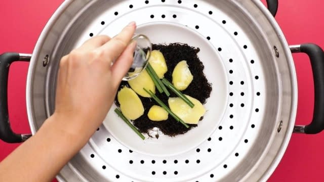 Pouring rice wine over black moss, ginger, and spring onion in steamer