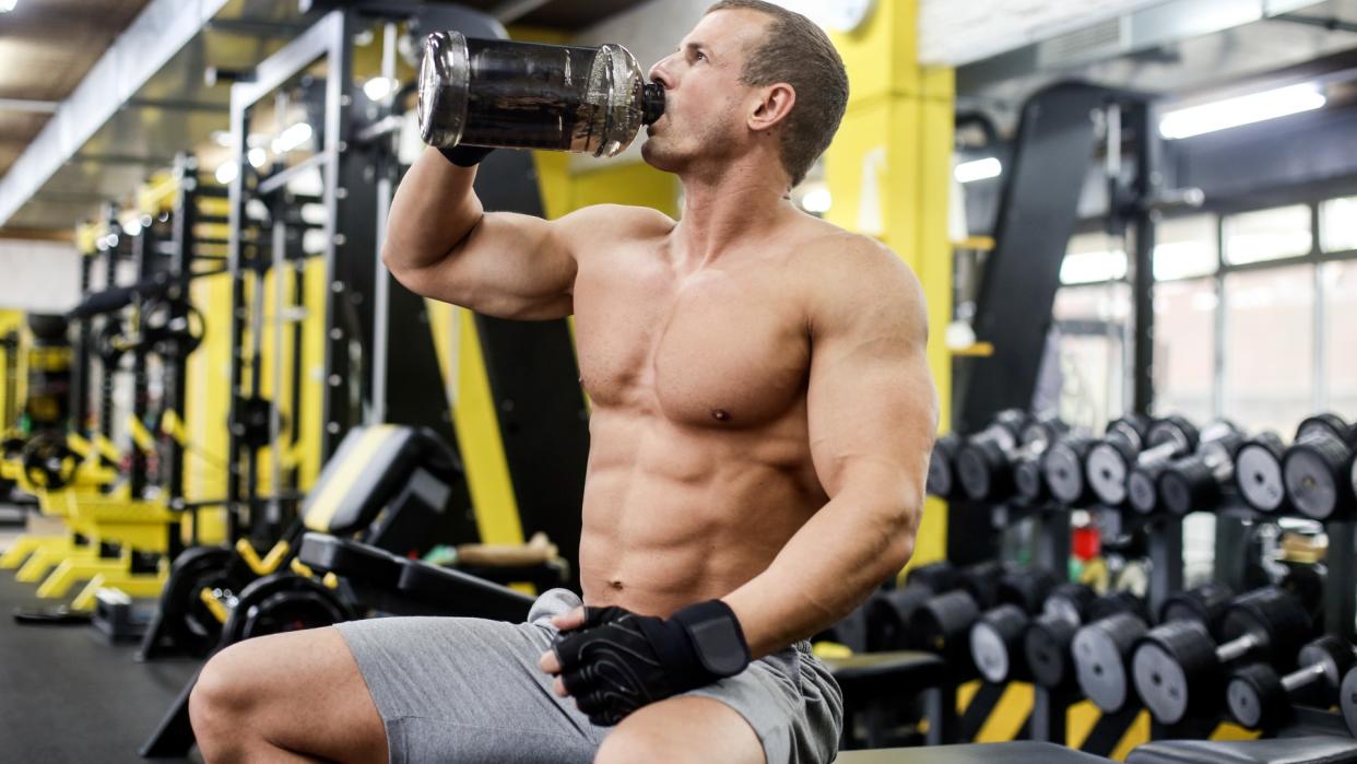  Man sitting on a workout bench drinking from protein shaker during resistance workout. 