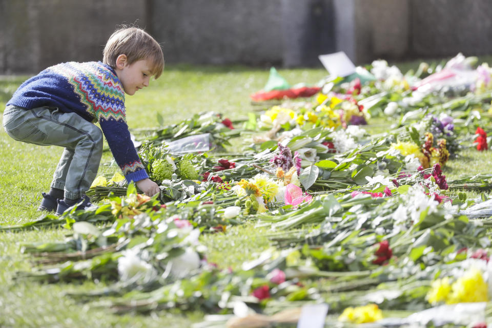 A child lays flowers outside the Cambridge gate of Windsor Castle in Windsor, England after the announcement regarding the death of Britain's Prince Philip, Friday, April 9, 2021. Buckingham Palace officials say Prince Philip, the husband of Queen Elizabeth II, has died. He was 99. Philip spent a month in hospital earlier this year before being released on March 16 to return to Windsor Castle. (AP Photo/Kirsty Wigglesworth)