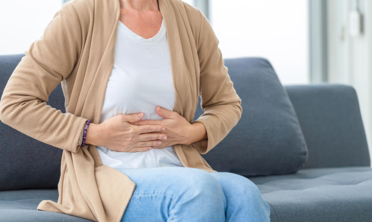 Unhappy woman stomach ache, mature woman with stomach pain feeling unwell sitting in living room