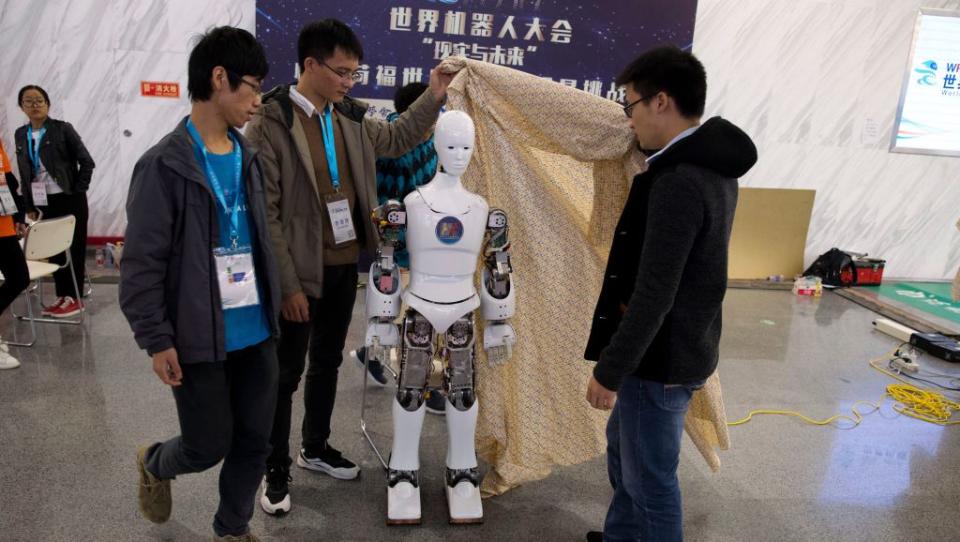 In this Friday, Oct. 21, 2016 photo, Chinese college students remove the cover from the Ares, a humanoid bipedal robot designed by them with fundings from a Shanghai investment company, displayed during the World Robot Conference in Beijing. China is showcasing its burgeoning robot industry as it seeks to promote use of more advanced technologies in Chinese factories and create high-end products that redefine the meaning of “Made in China.” The Ares is a human-sized robot they designed with exposed metal arms and hands and a wide range of uses in mind, from the military to performing basic tasks in a home. (AP Photo/Ng Han Guan)