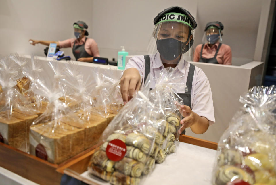 Employees wearing gear to protect against the new coronavirus outbreak arrange bread on display at a bakery in Jakarta, Indonesia, Wednesday, June 3, 2020. (AP Photo/Dita Alangkara)