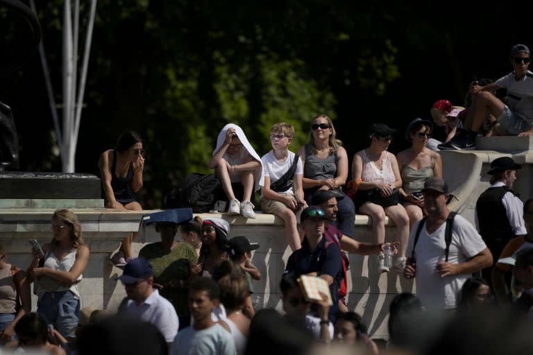 Los turistas esperan bajo el sol para ver la ceremonia de cambio de guardia fuera del Palacio de Buckingham, durante el clima caliente en Londres, el lunes 18 de julio de 2022.