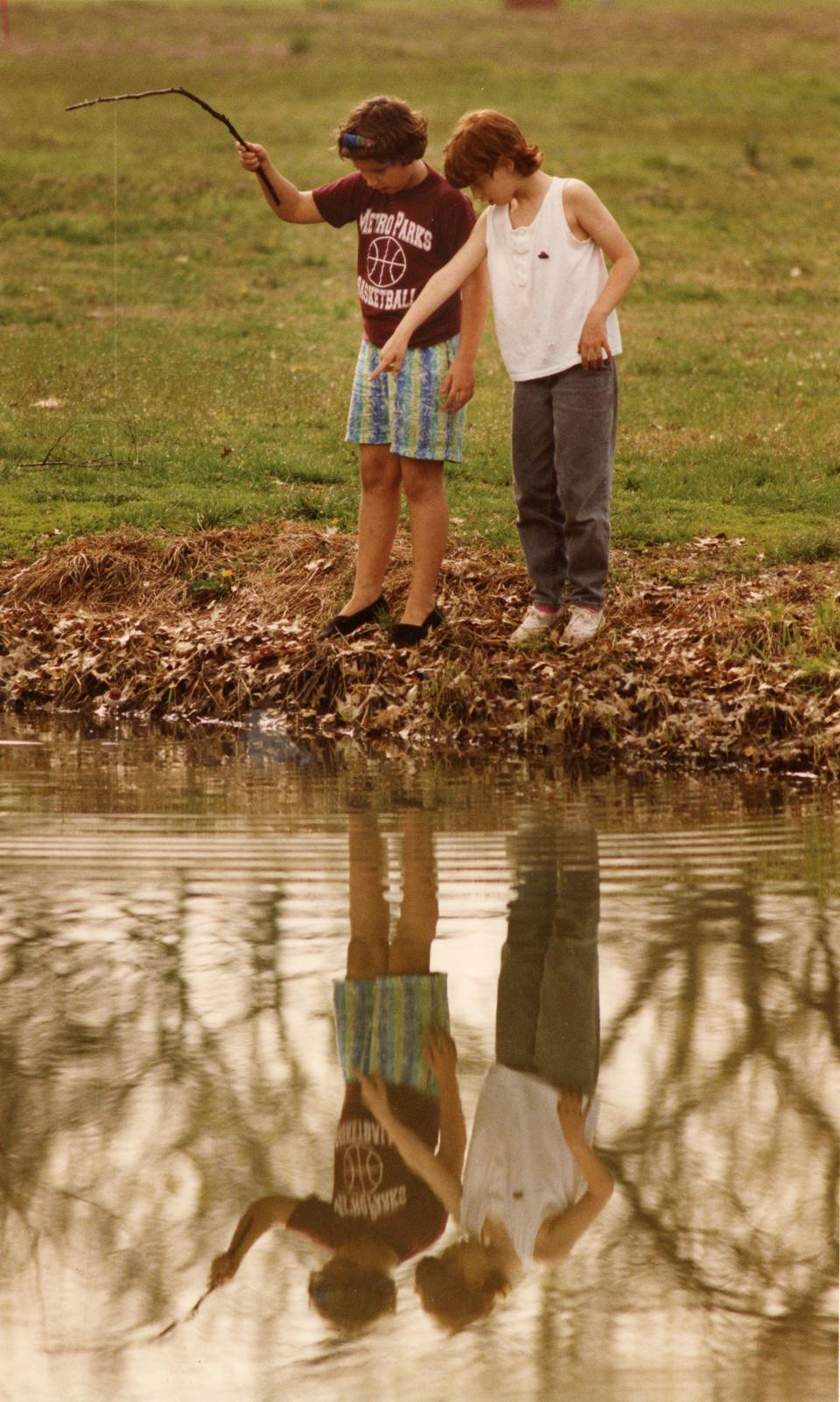 Melanie Nokes, 10, and her sister Serena Nokes, 8, hunt for fishing bait in the pond at Chickasaw Park in 1992. They plan to fish with sticks and rope after finding some bait.