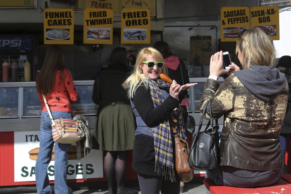 In a Saturday March 30, 2013, photo a visitor to New York's Coney Island poses holding a corn dog. Despite making the traditional Palm Sunday opening, many of the seasonal businesses at Coney Island are still reeling from the aftermath of Superstorm Sandy. (AP Photo/Mary Altaffer)