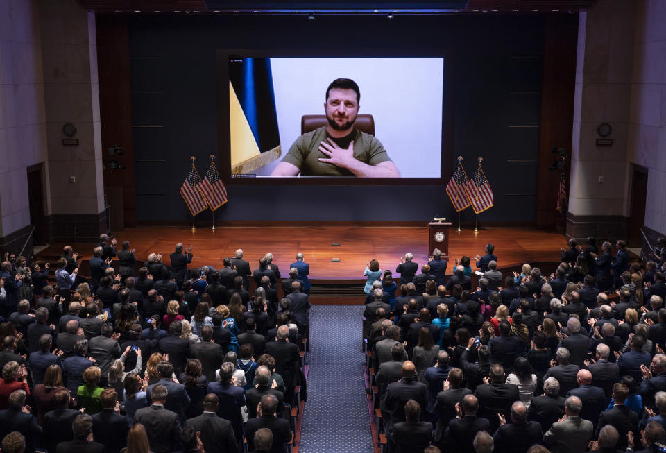 Congress members watch Volodymyr Zelensky on a large video screen flanked by American flags.