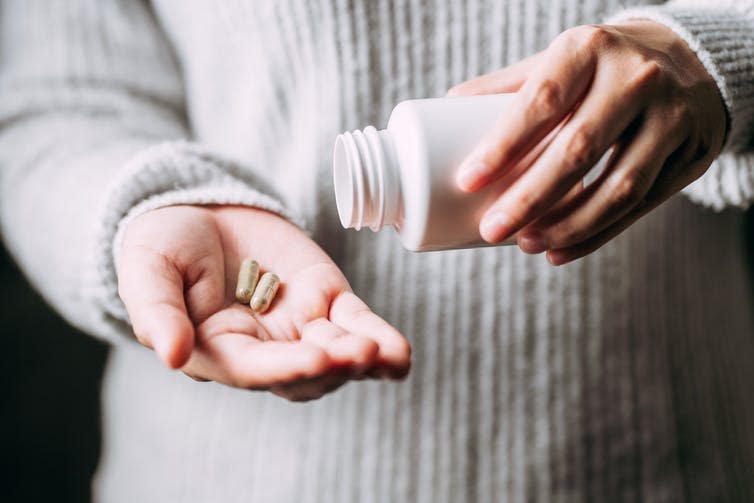 A person's hands. One hand is open with two tablets held in the palm, while the other holds a medicine bottle.