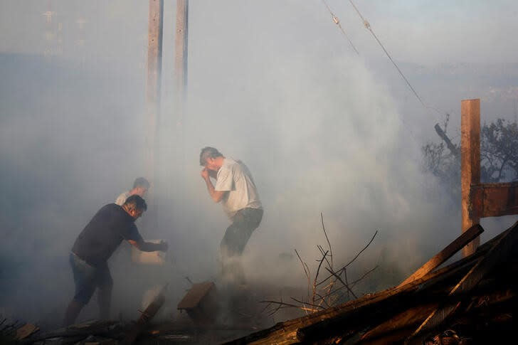 Un hombre vierte agua sobre los restos de una casa quemada durante un incendio forestal en Viña del Mar, Chile