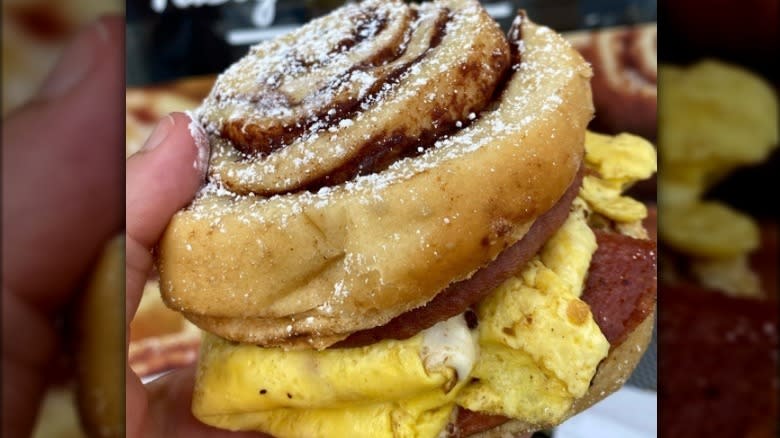 Hand holding a breakfast sandwich made with morning buns