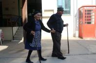 Maronite husband and wife Iosif (92) and Chrystalla (93) hold hands as they walks outside a coffee shop in Kormakitis