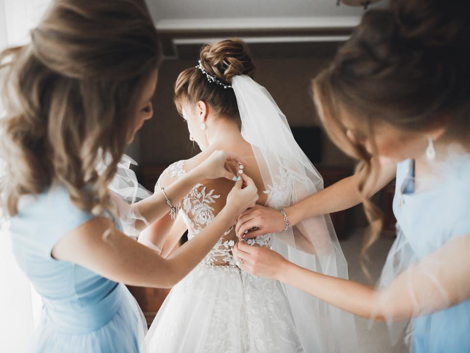 bridesmaids in blue helping a bride button up her dress for wedding