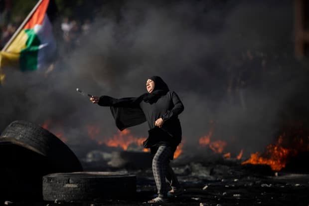 A Palestinian woman throws a rock toward Israeli forces at the Hawara checkpoint, south of the West Bank city of Nablus, Tuesday. Protests and clashes in the occupied territory have spread and so far claimed at least 12 lives.