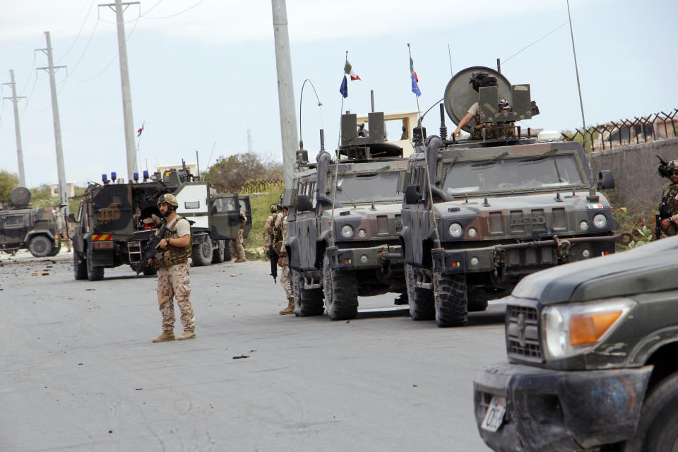 A member of the Italian military stands next to a damaged armored personnel carrier after an attack on a European Union military convoy in the capital Mogadishu, Somalia Monday, Sept. 30, 2019. A Somali police officer says a suicide car bomber has targeted a European Union military convoy carrying Italian military trainers in the Somali capital Monday. (AP Photo/Farah Abdi Warsameh)