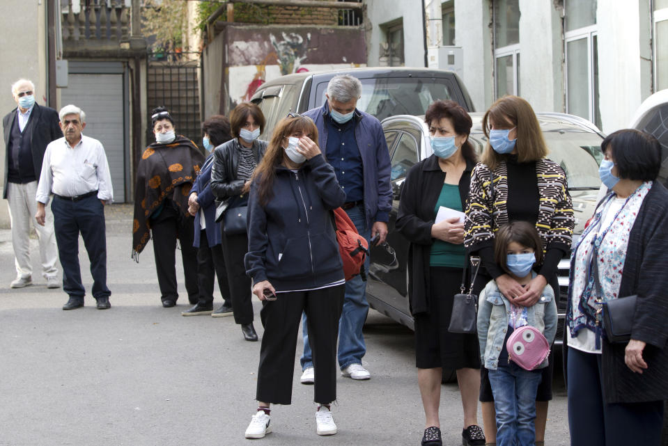 Georgians wearing face masks to help curb the spread of the coronavirus, lineup to vote outside at a polling station during the parliamentary elections in Tbilisi, Georgia, Saturday, Oct. 31, 2020. The hotly contested election between the Georgian Dream party, created by billionaire Bidzina Ivanishvili who made his fortune in Russia and has held a strong majority in parliament for eight years, and an alliance around the country's ex-president who's in self-imposed exile in Ukraine. (AP Photo/Shakh Aivazov)