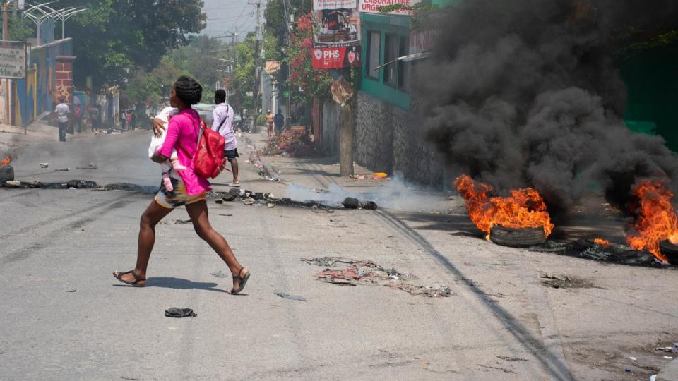 PHOTO: A woman carrying a child runs from the area after gunshots were heard in Port-au-Prince, Haiti, on March 20, 2024.  (Clarens Siffroy/AFP via Getty Images)