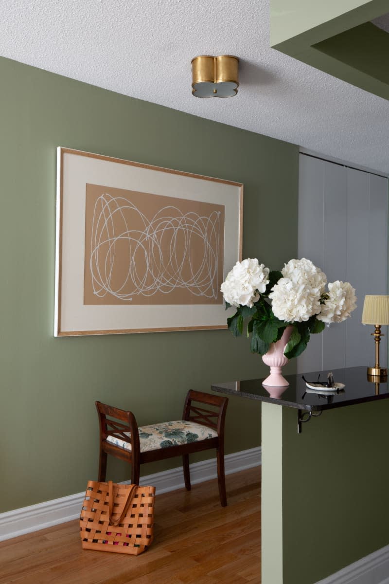 Green wall entry way with peninsula counter half wall separating entry, vintage wood bench with floral upholstery