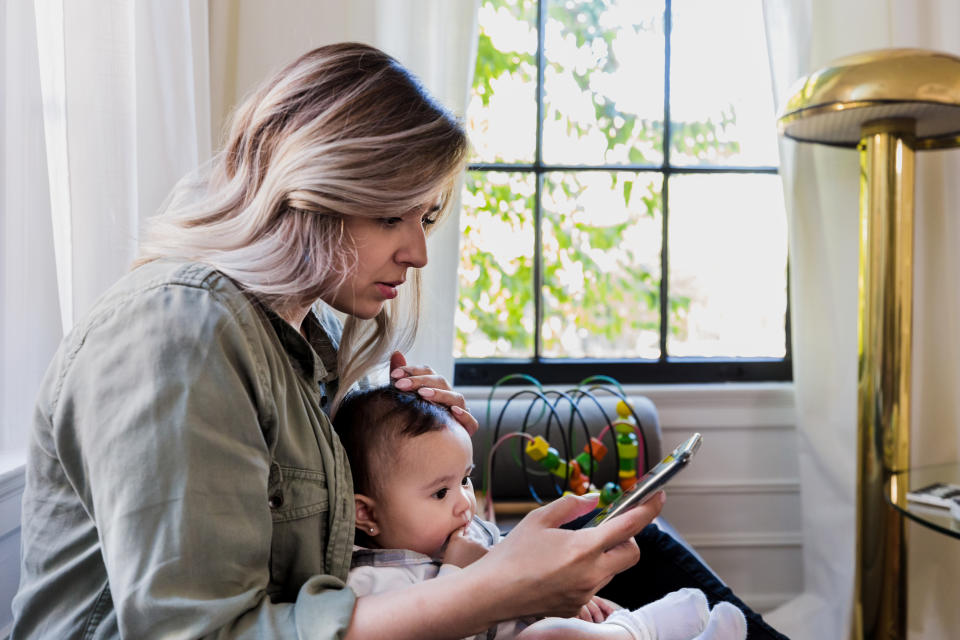 The worried mid adult mother uses her smart phone to find information about illness in babies.