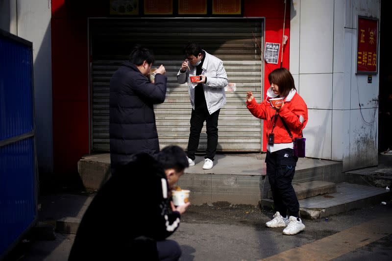 People eat their breakfast near a closed store and a barricade in Wuhan