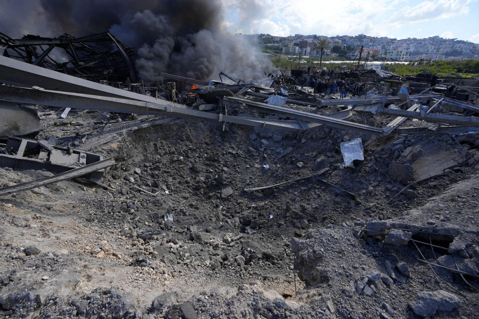 People gather near a hole caused by Israeli airstrikes that was attacked a warehouse on Monday, at an industrial district in the southern coastal town of Ghazieh, Lebanon, Tuesday, Feb. 20, 2024. Israeli warplanes carried out at least two strikes near the southern port city of Sidon in one of the largest attacks near a major city, wounding a dozen of people, Lebanese state media said. (AP Photo/Bilal Hussein)