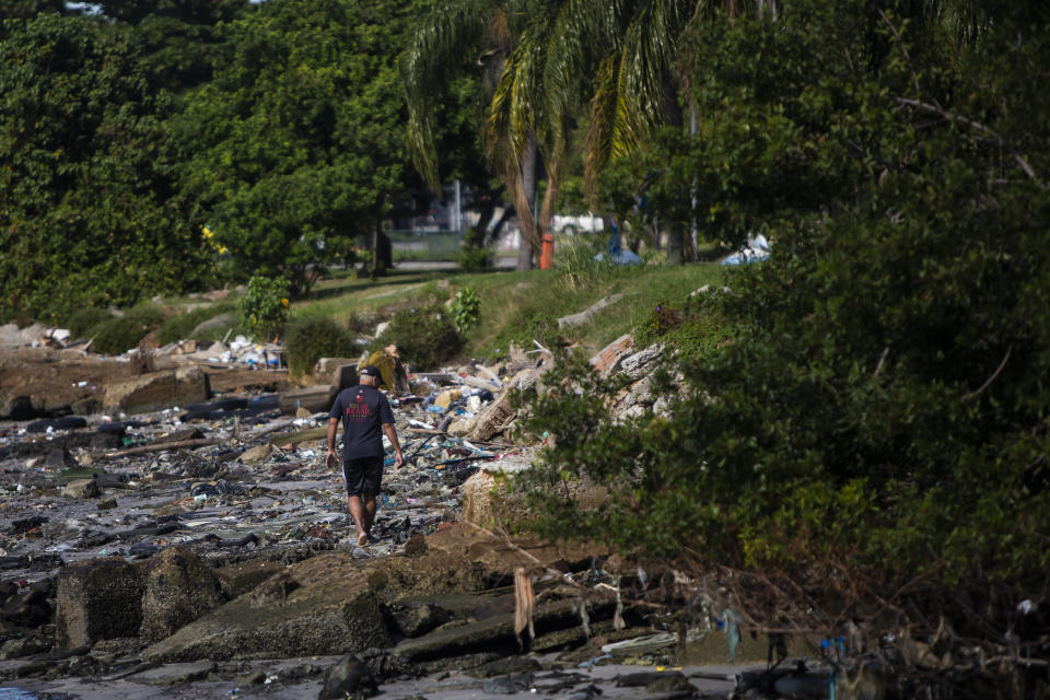 A man walks on the banks of the Guanabara Bay littered with garbage, in Rio de Janeiro, Brazil, Thursday, June 24, 2021. The bay waters where the the 2016 Rio de Janeiro Olympics sailing competitions took place have not been cleaned of sewage, as had been promised. (AP Photo/Bruna Prado)