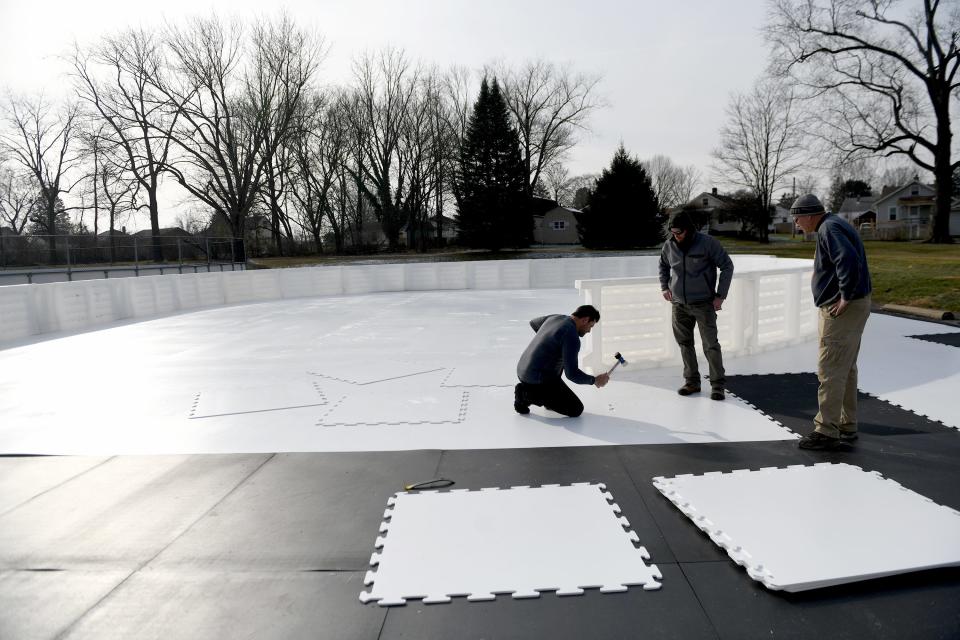 Chris Crowley, left, with Global Synthetic Ice, along Massillon Parks and Recreation maintenance supervisor Chris Moser, center, and Superintendent Joe Pape, build a skating rink in Wampler Park. The rink opens Tuesday.